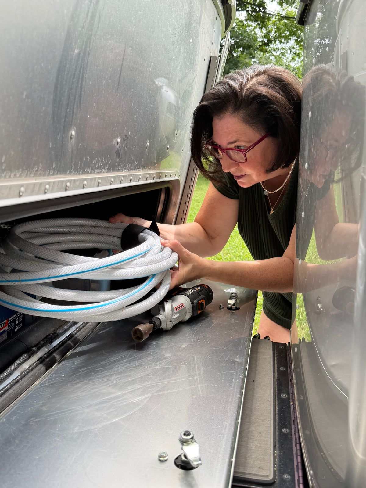 Jennifer Eggers working with RV hoses inside an Airstream exterior compartment